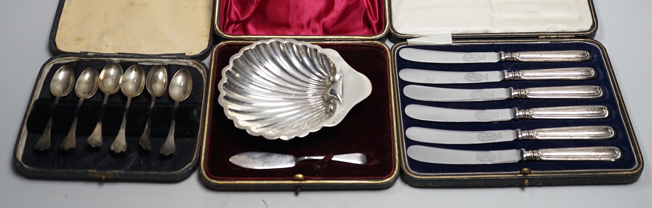 A set of six tea knives, an Edwardian silver butter shell and knife and a set of six silver coffee spoons, all cased.